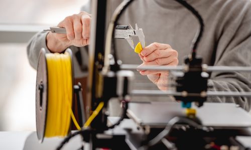 Man holding in his hands yellow plastic detail printing with 3D printer and measuring it